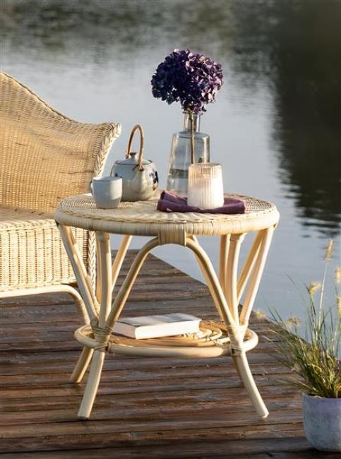 Preview: Rattantisch auf einem Holzuntergrund an einem See, mit einer Vase, einer Teekanne, einer Tasse und einem Glaswindlicht